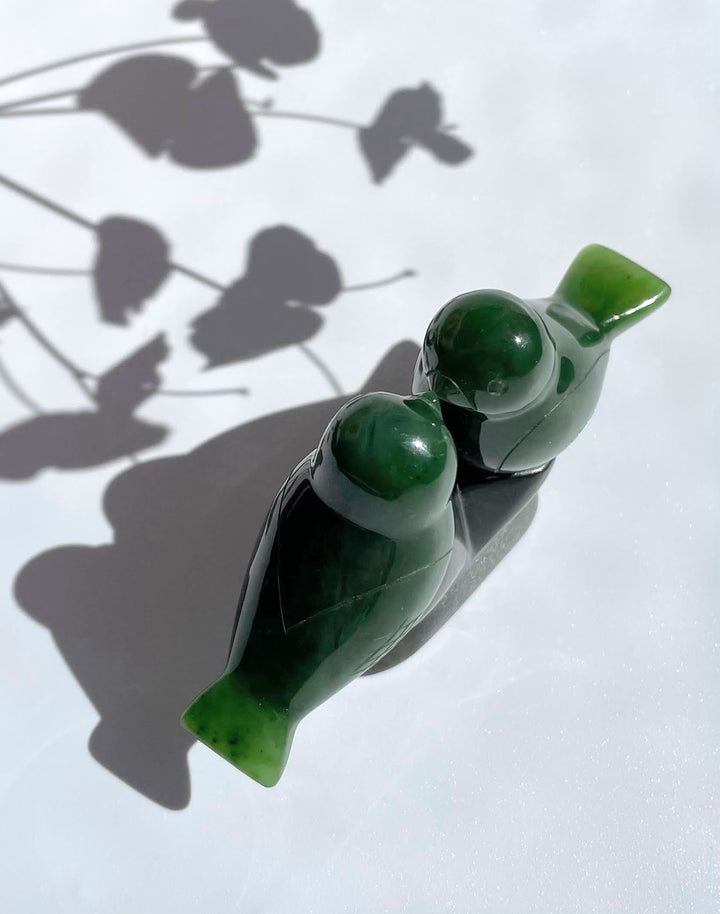 Two green lovebird figurines on a glossy black base viewed from above.