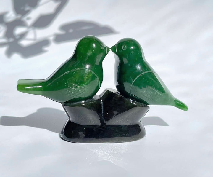 Two green lovebird figurines perched on a dark base facing each other.