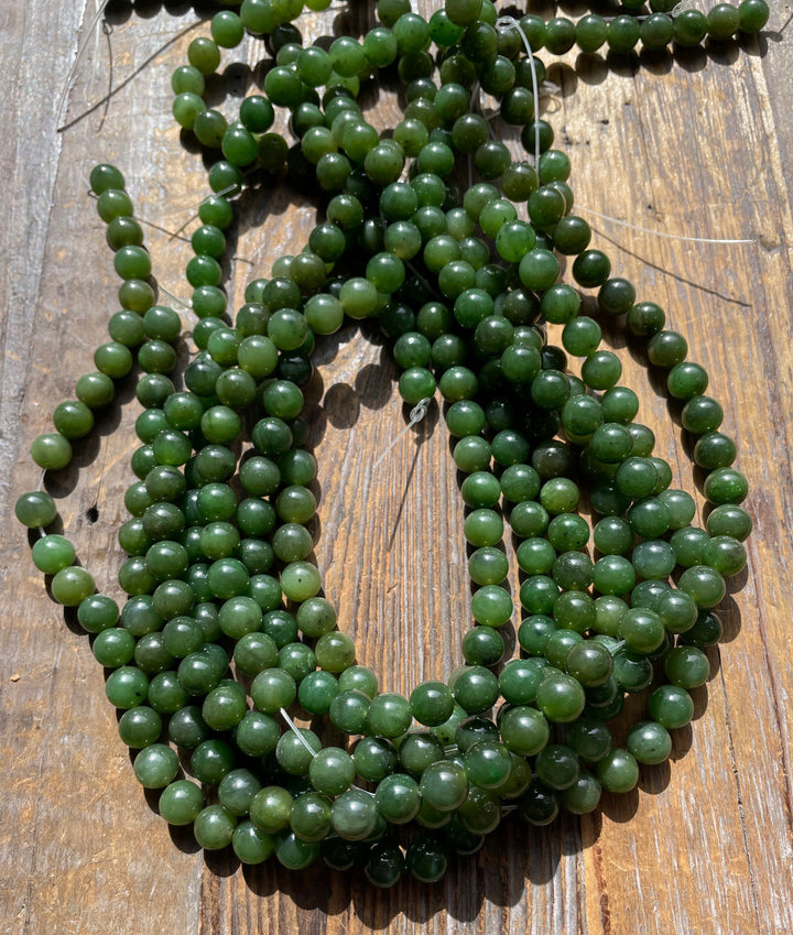 Multiple strands of 8mm carving grade Canadian jade beads piled on a wooden surface.