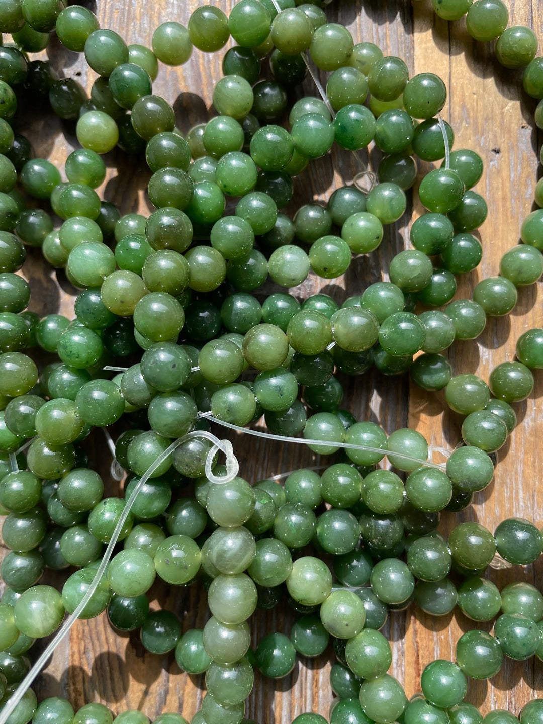 Close up of green 8mm carving grade Canadian jade beads scattered on a wooden surface
