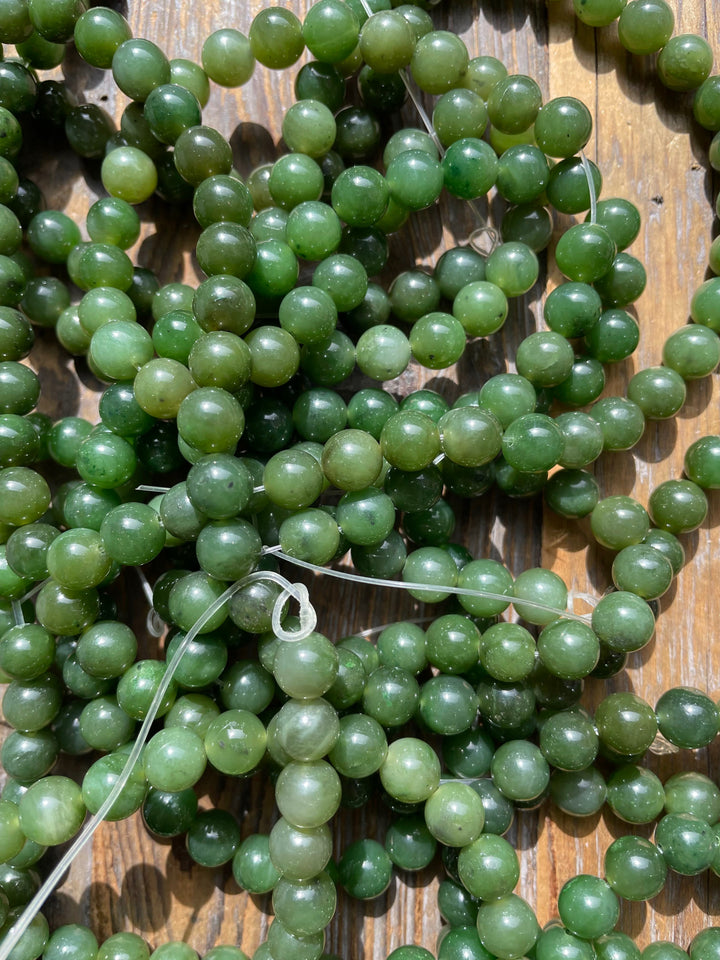 Close up of green 8mm carving grade Canadian jade beads scattered on a wooden surface