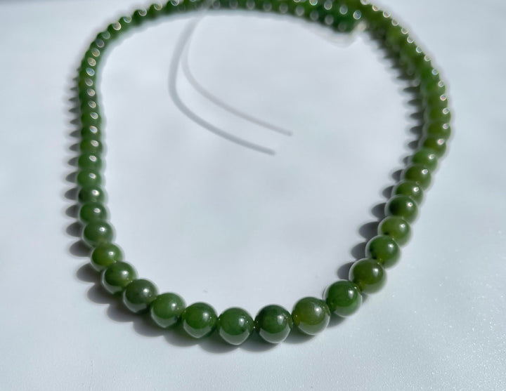 Close up of glossy green 6mm beads arranged on a curved unstrung 16 inch strand