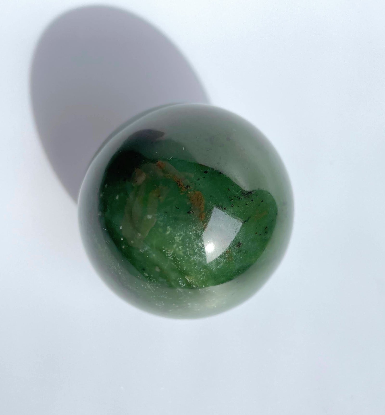 Top view of a polished green jade sphere showing internal swirls and inclusions against a white background