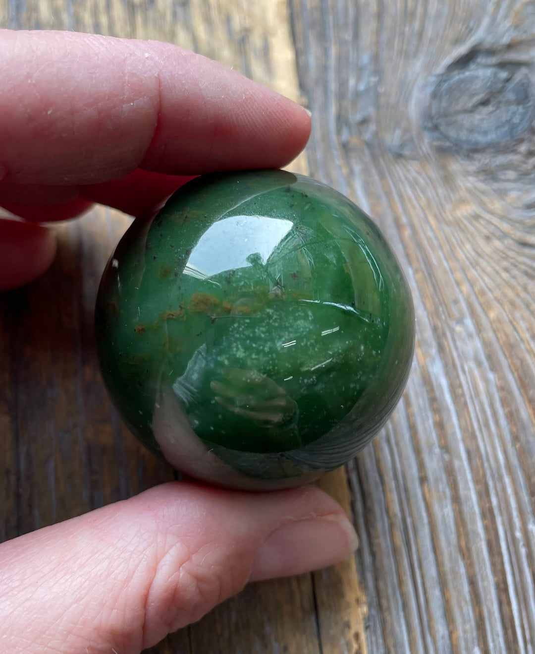 Green polished Canadian jade sphere, 40mm, held between fingers.