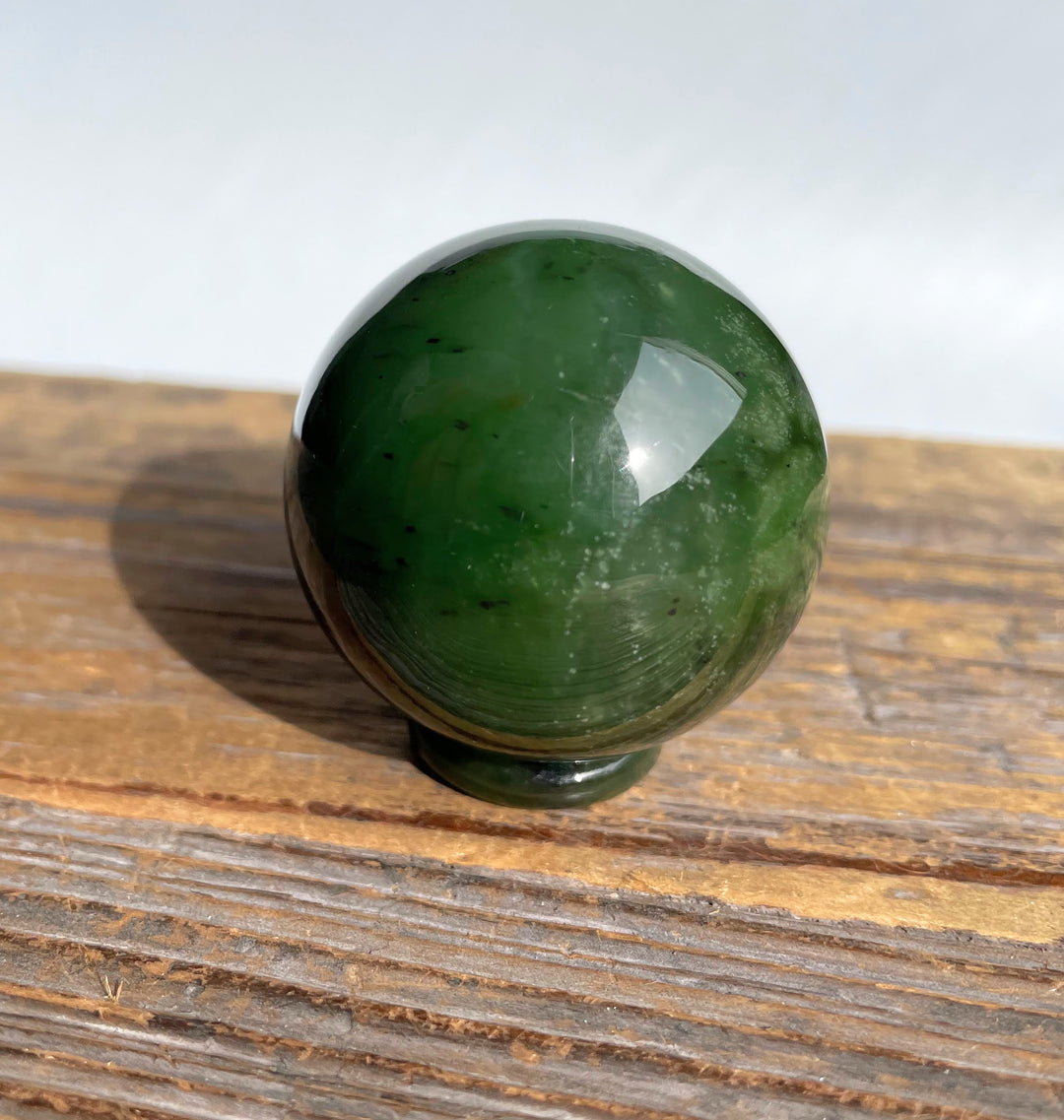 Green Canadian jade sphere resting on a wooden surface, 40mm diameter.