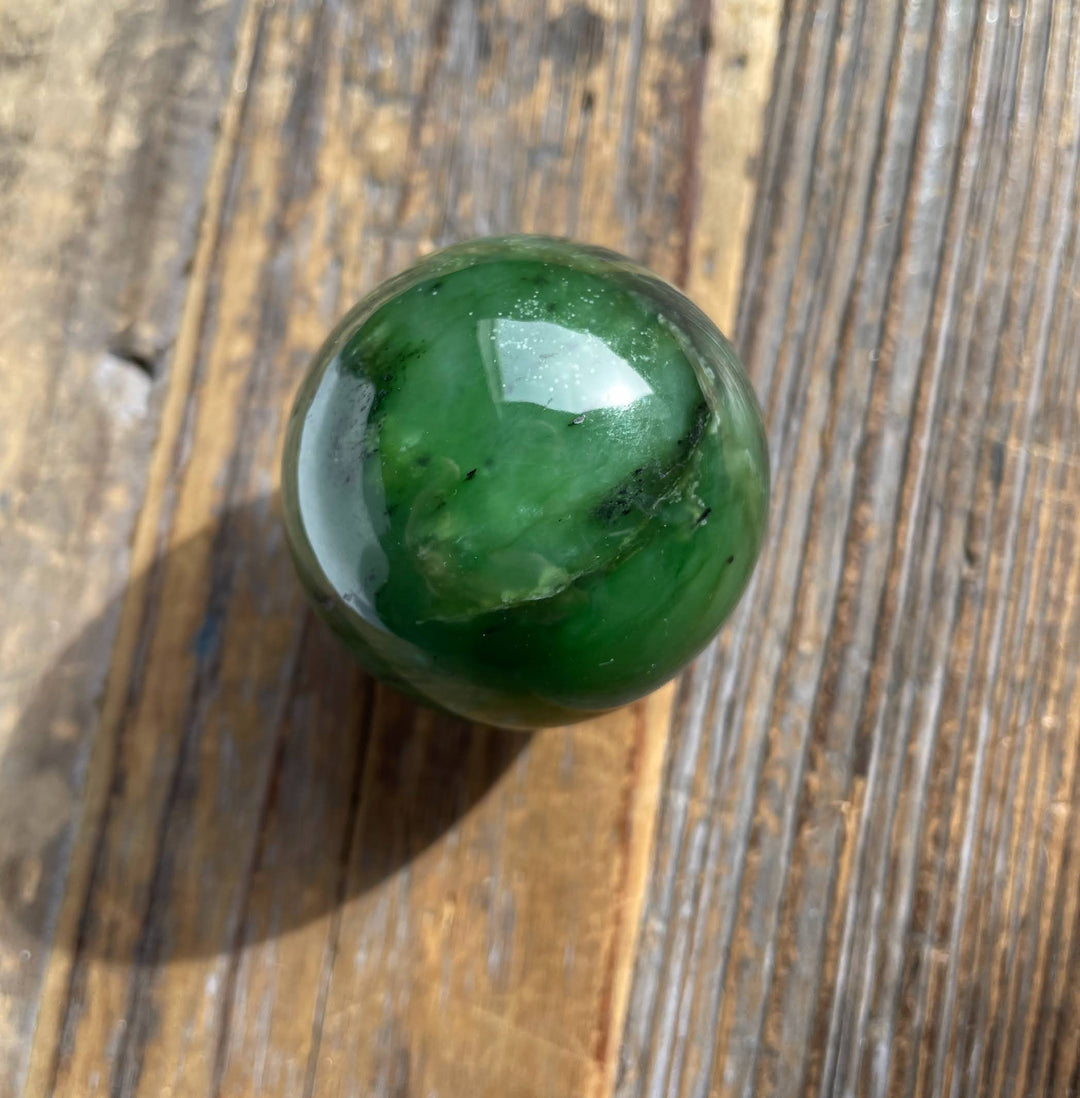 Top-down view of a 40mm green Canadian jade sphere on a wooden surface.