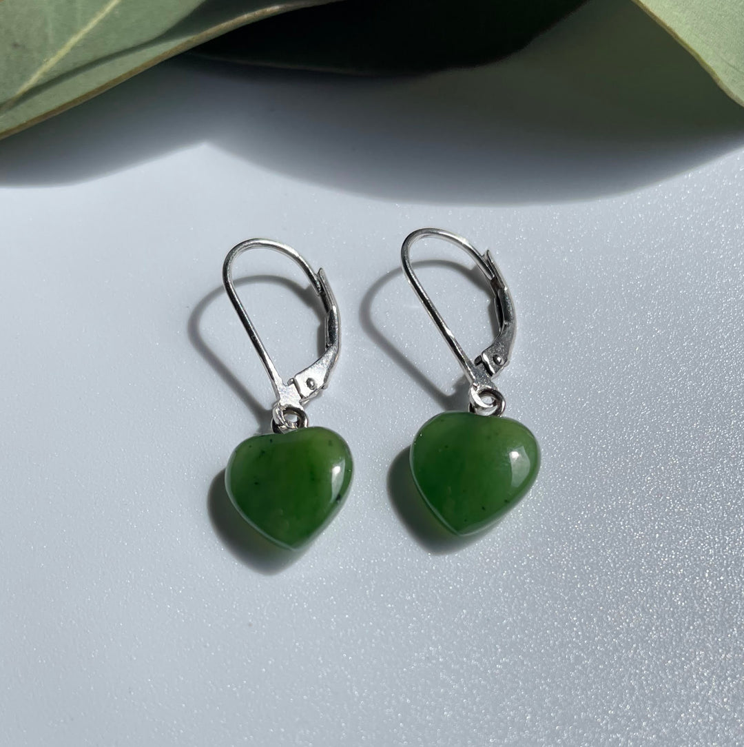 Close-up view of jade heart earrings with silver hooks on a white surface.