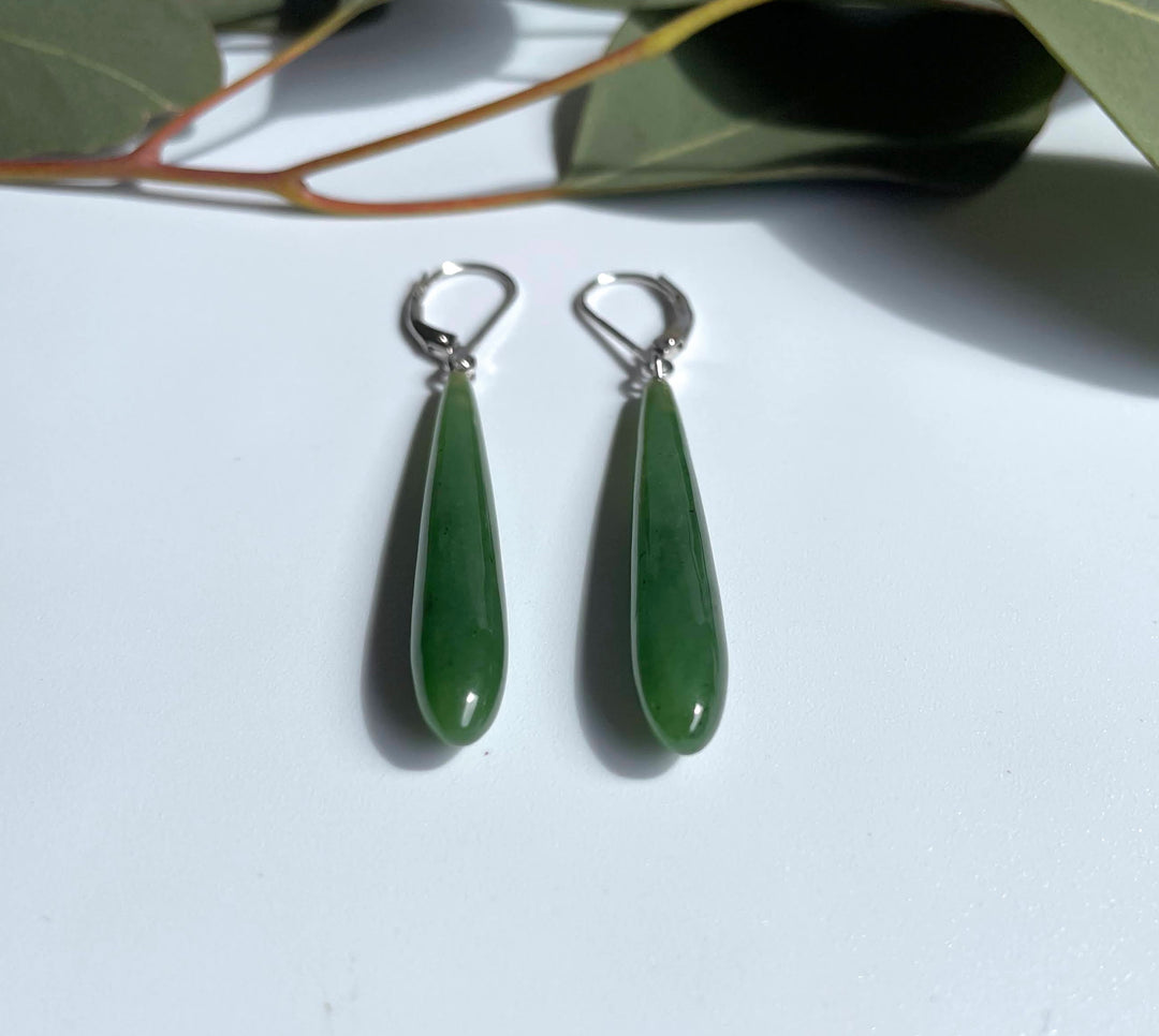 Long jade drop earrings with gold lever-back closures on white surface with leaves in background.