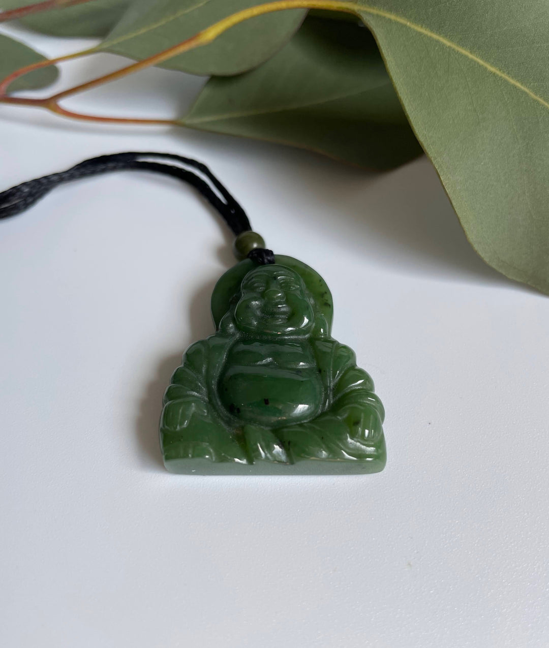 Green jade Buddha pendant on a black cord shown against a white background