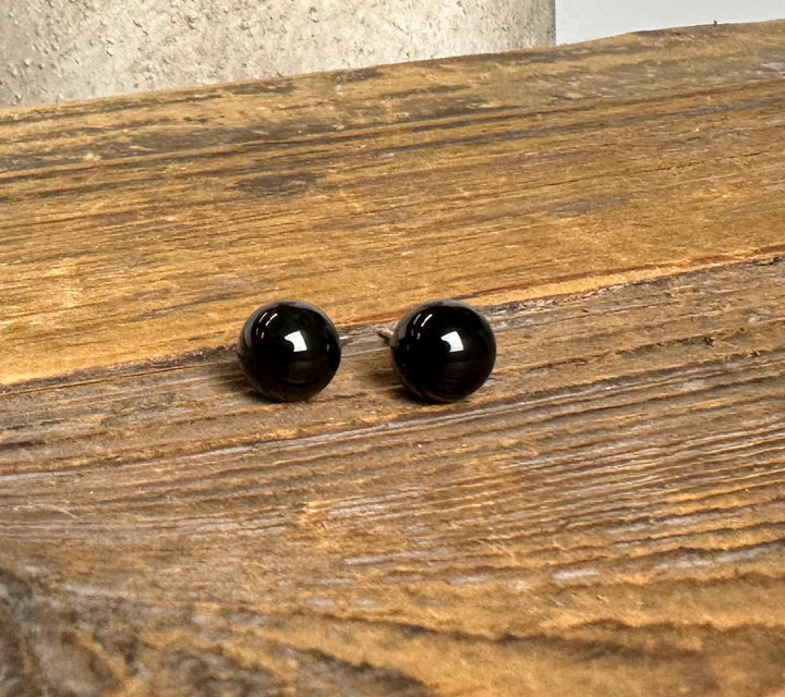 Two black jade sphere stud earrings with silver posts laid on a wooden surface