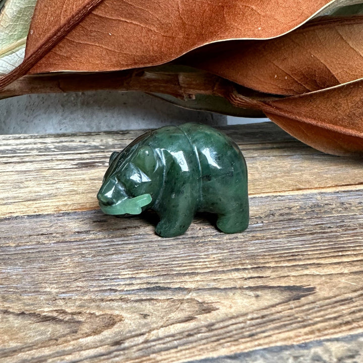 Dark green jade bear carving with a lighter green jade fish in its mouth on a wooden surface