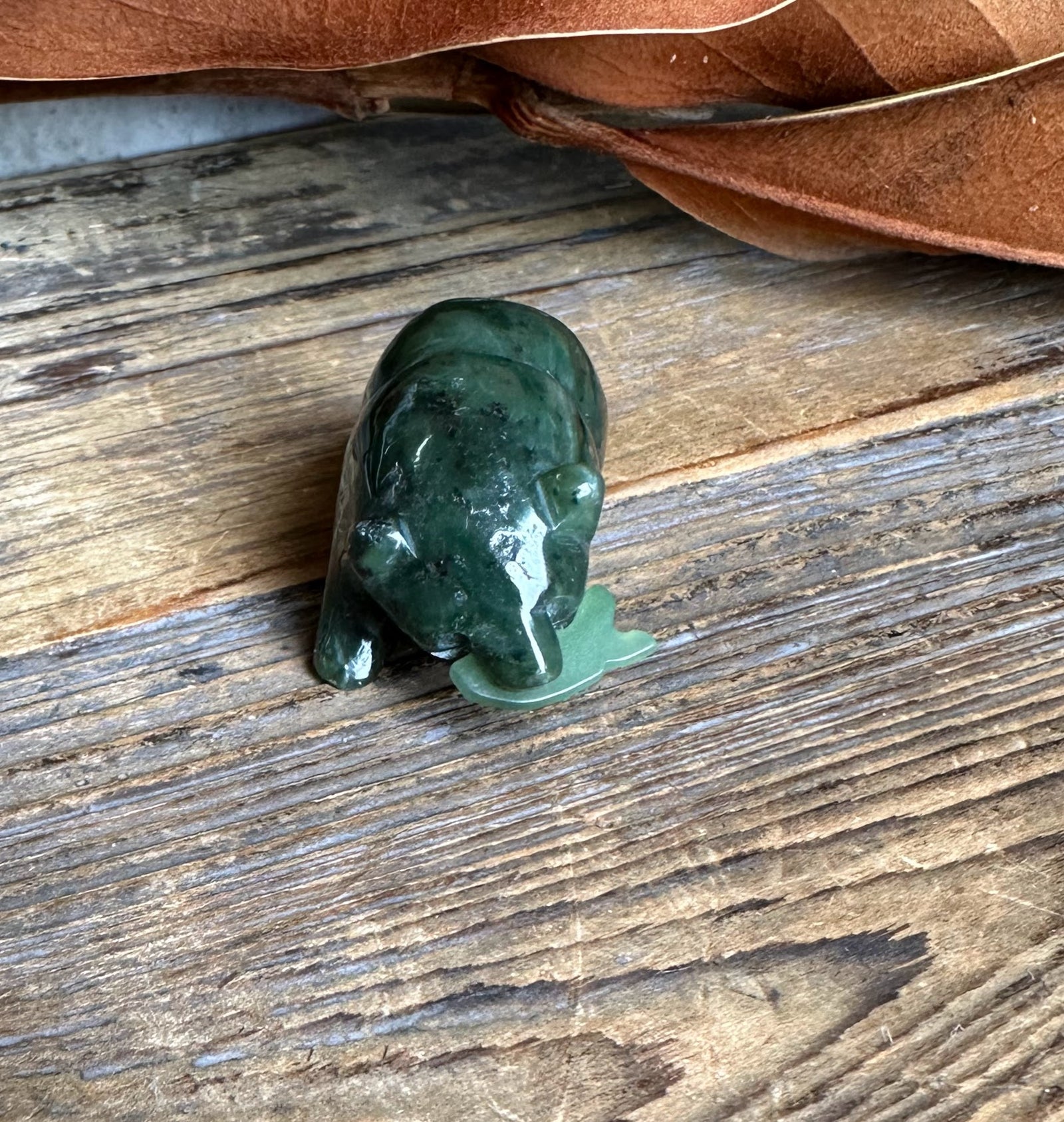 Dark green jade bear with a small jade fish beside it on a rustic wooden surface