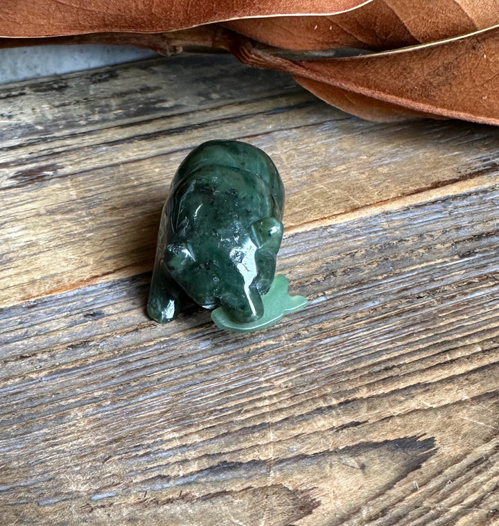 Dark green jade bear with a small jade fish beside it on a rustic wooden surface
