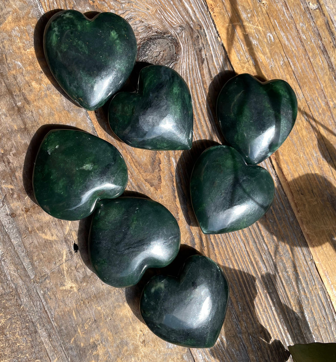 Group of dark green jade satin heart shaped stones arranged on a weathered wooden surface