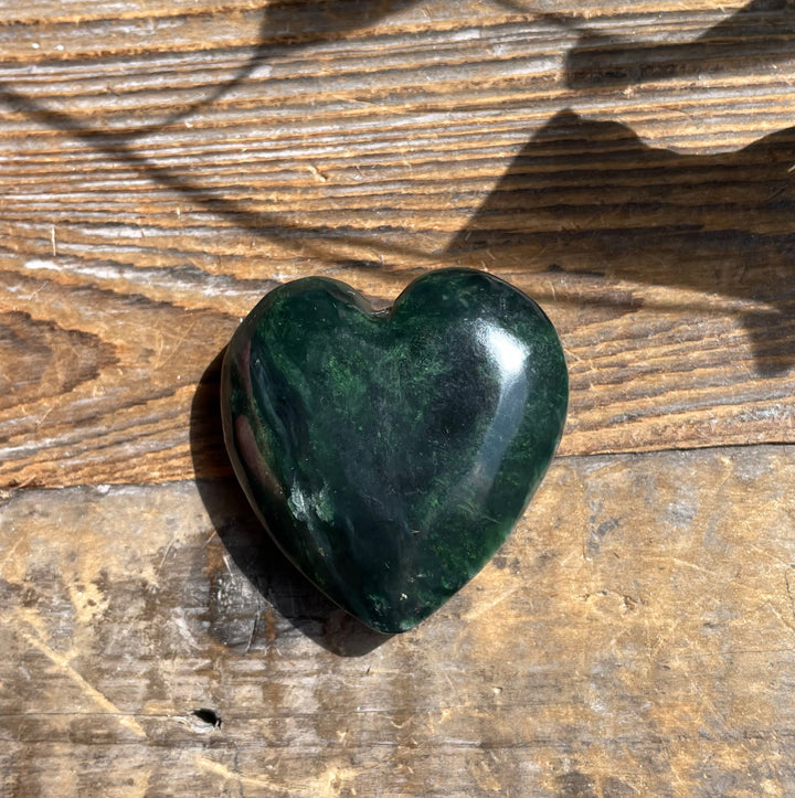Dark green jade satin heart pendant on a necklace chain laid on sunlit wood background