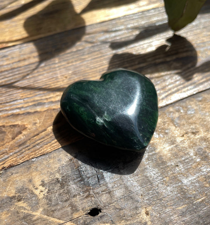 Close up of dark green jade satin heart pendant on a wooden surface