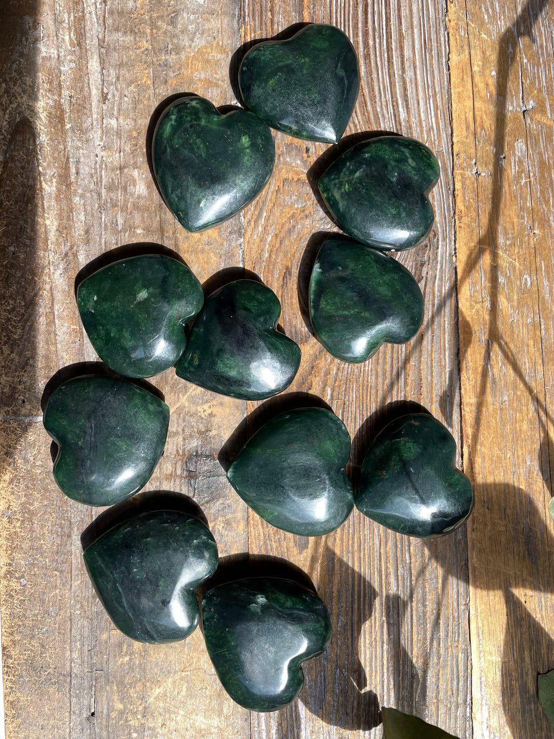 Several dark green jade satin heart shaped stones scattered on a wooden surface
