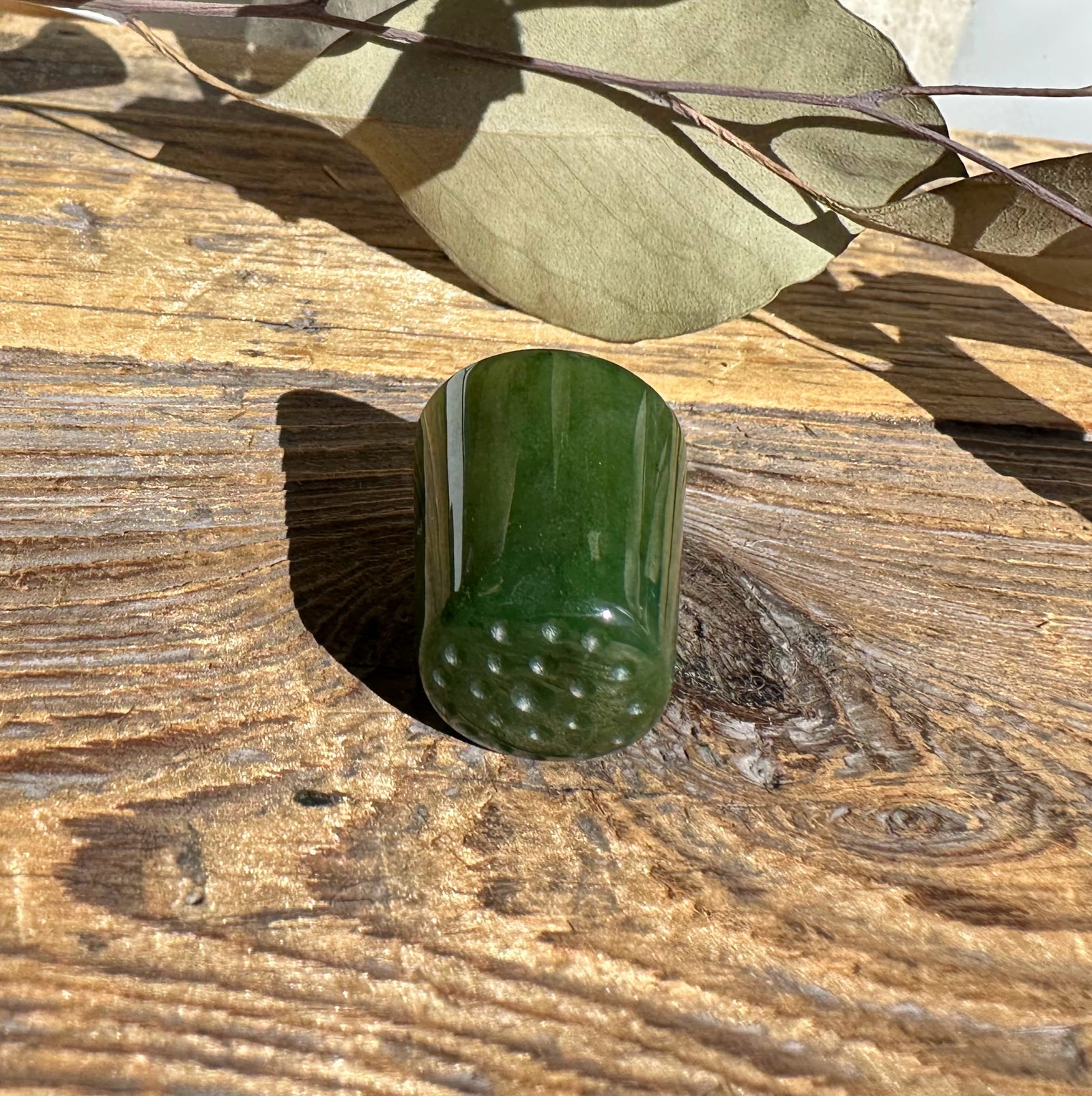 Green glossy thimble with raised dimples around its base on a weathered wooden surface