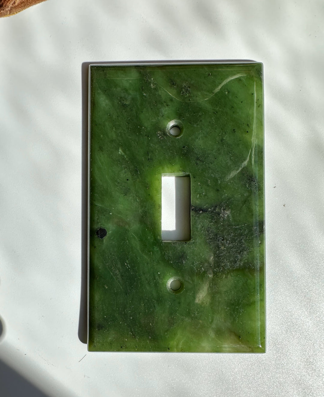 Green marble traditional light switch plate with a vertical rectangular opening for a switch.