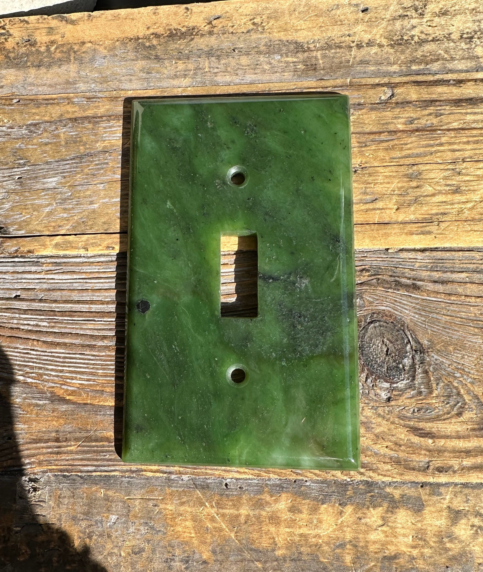 Green marble patterned traditional light switch plate with central rectangular opening and two screw holes on a wooden surface.