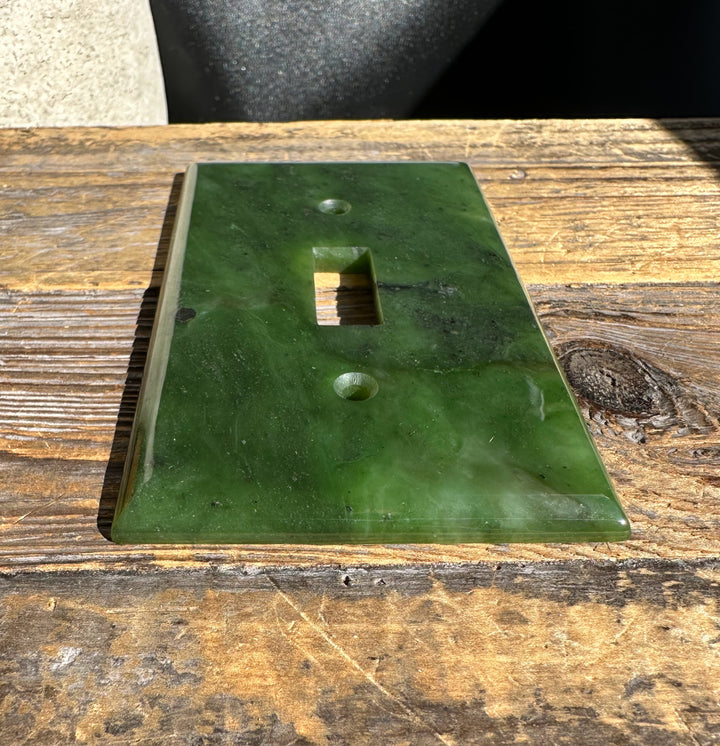 Green marble pattern traditional light switch plate with vertical slot and two screw holes, angled view.
