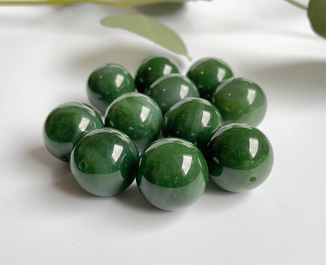 Polished green jade beads with drilled holes arranged in a cluster on a white surface