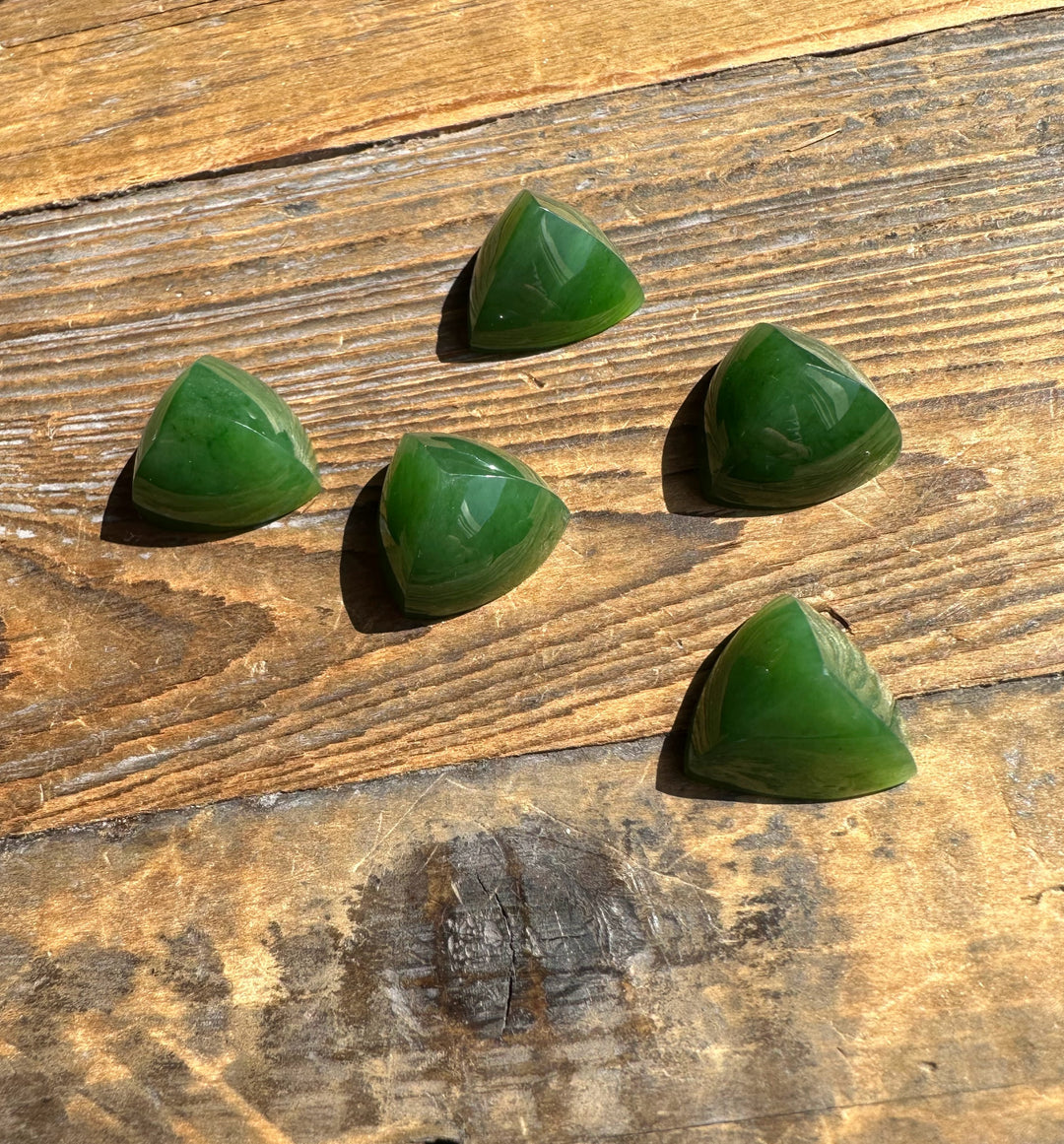 Five green jade pyramid cabochons on a rustic wooden surface
