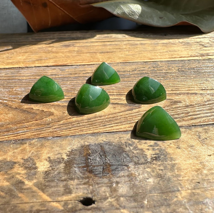Five AA Canadian jade pyramid cabochons on a rustic wooden surface