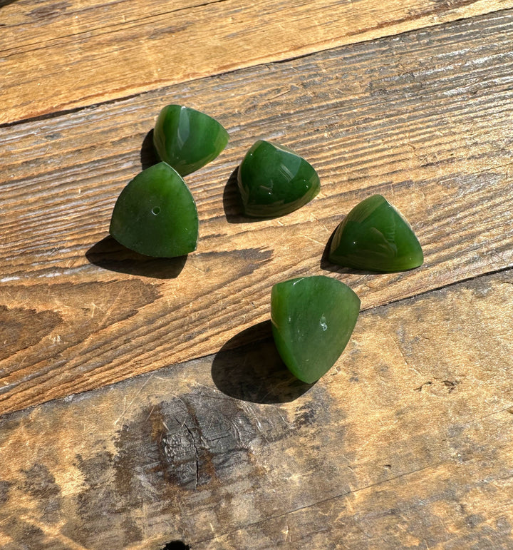 Five green jade pyramid cabochons with flat backs on wood, one showing a small hole
