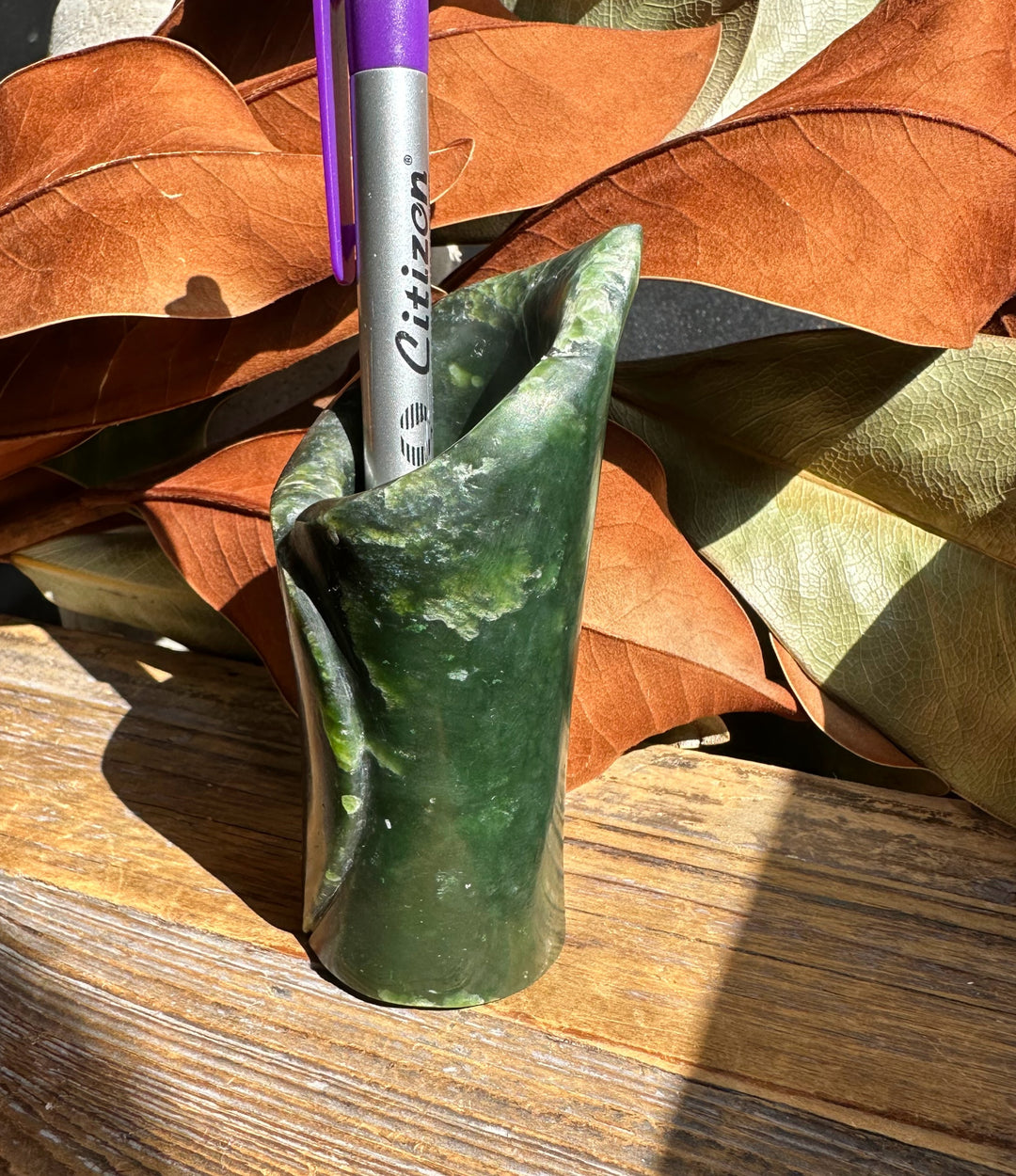 Green jade pen holder with folded rim and purple pen inserted on a wooden surface.