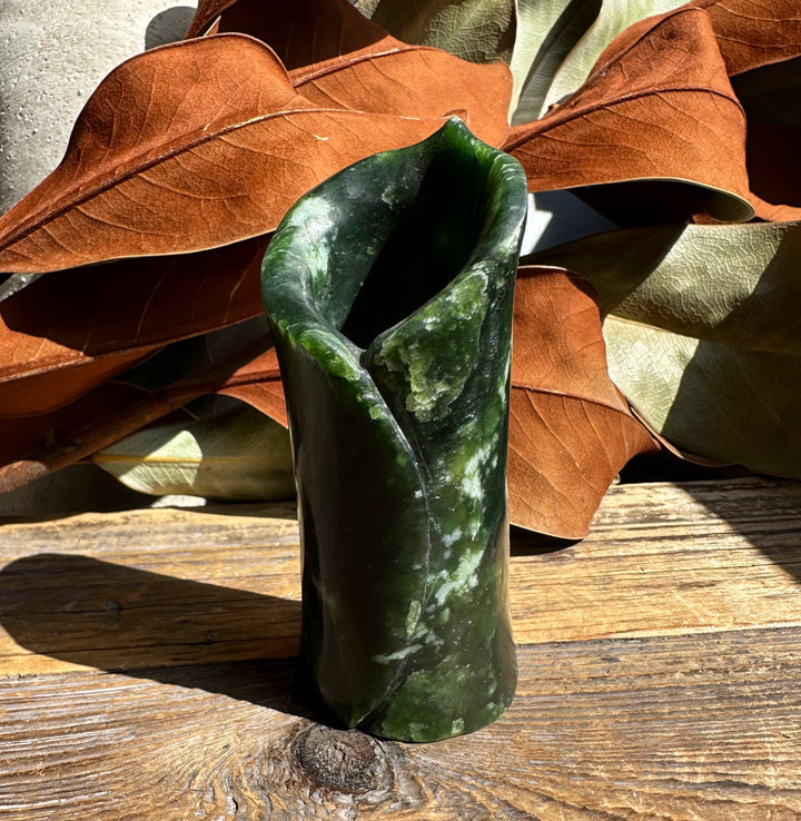 Deep green jade vase with a curved opening, set against brown autumn leaves.