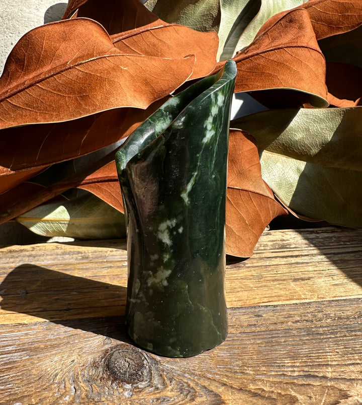 Jade pen holder vase in dark green with white marbling on sunlit wood.