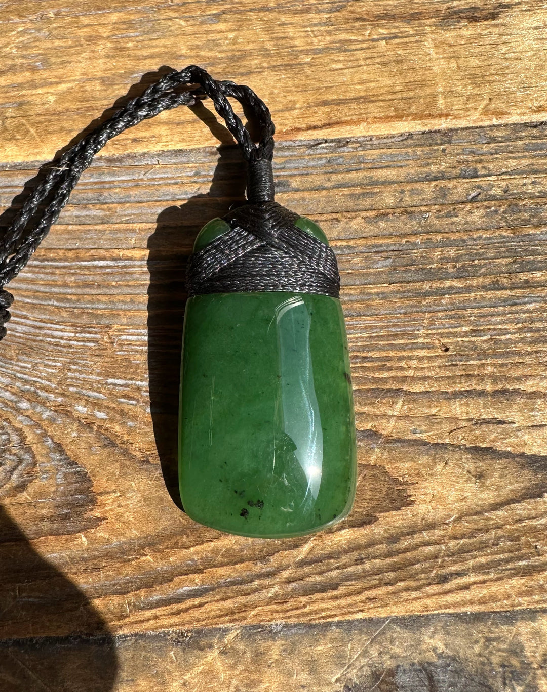 Green jade pendant wrapped in black cord with braided loop on a wood surface