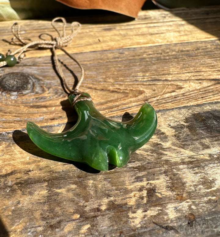 Close-up of green manta ray pendant with cord on weathered wooden surface.