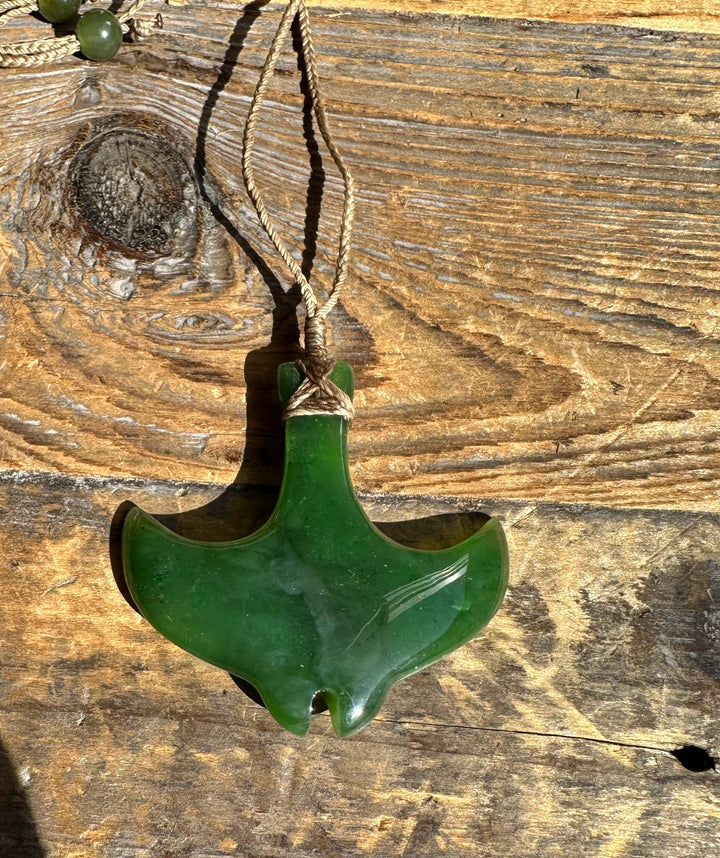 Green manta ray pendant on a beige braided cord against weathered wood
