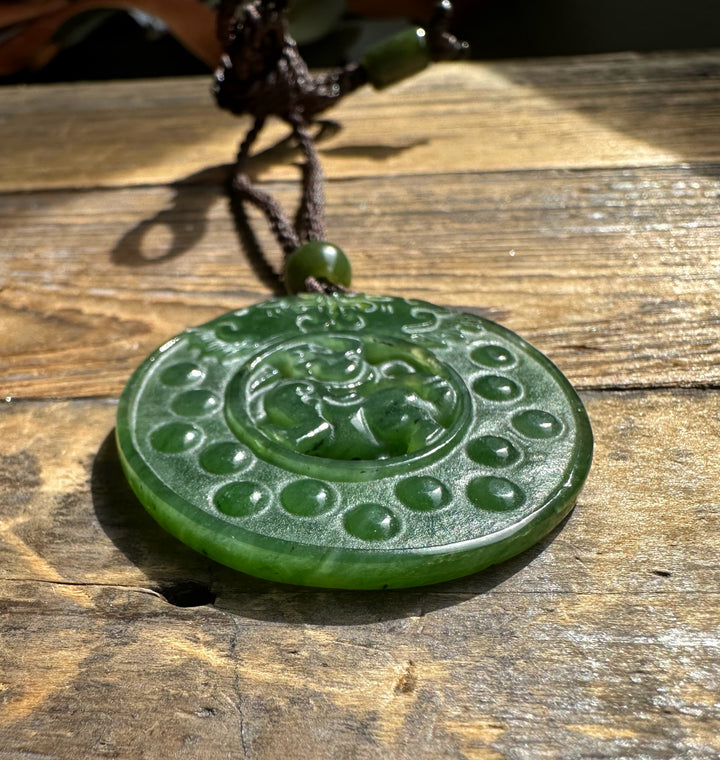 Close-up of green jade Pixiu pendant on braided brown cord with a bead resting on a wooden surface