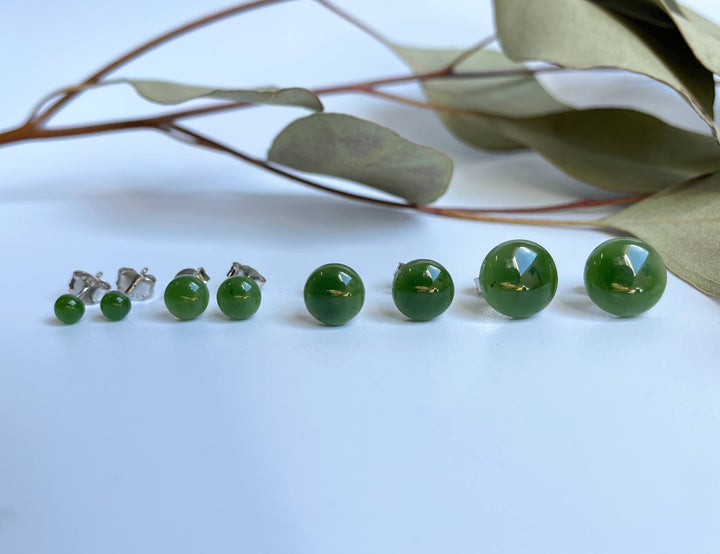 Green jade flat stud earrings in multiple sizes arranged in a row on a white surface