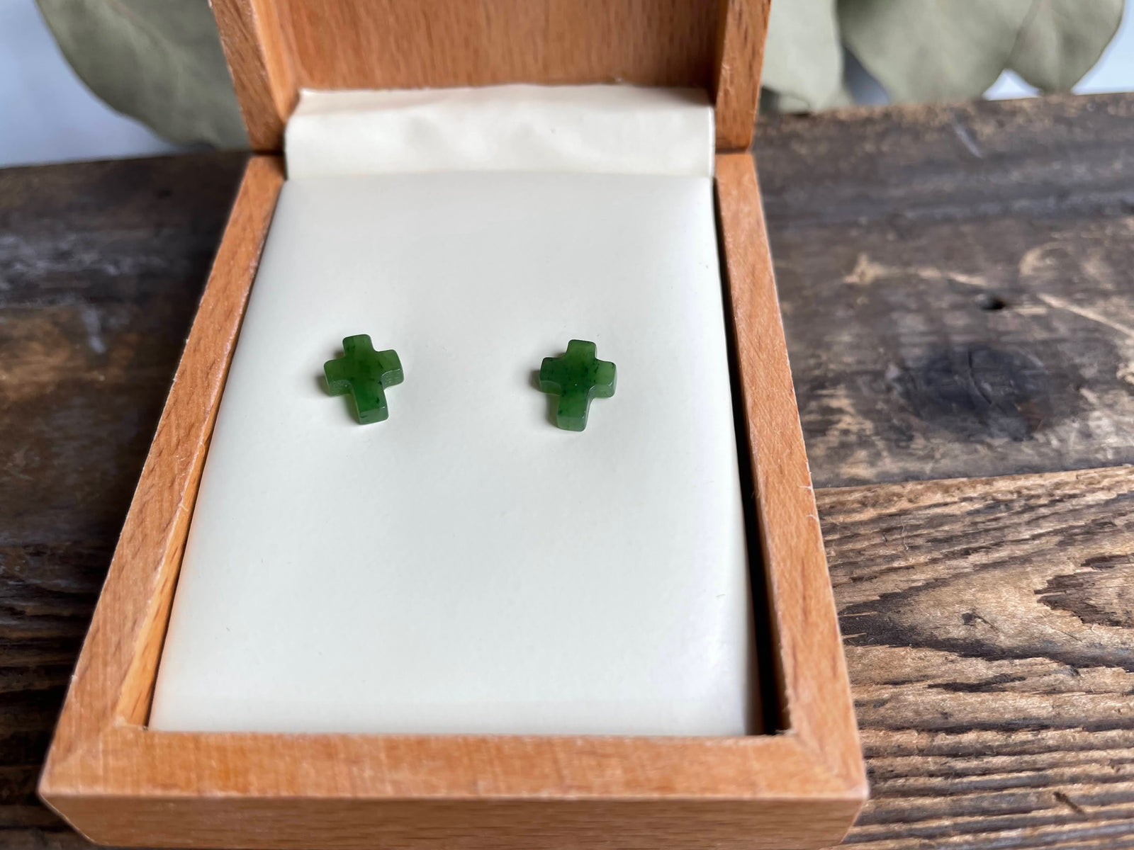 Pair of small jade cross earrings on a white display pad inside an open wooden box.
