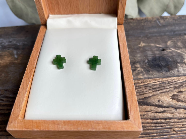 Pair of small jade cross earrings on a white display pad inside an open wooden box.