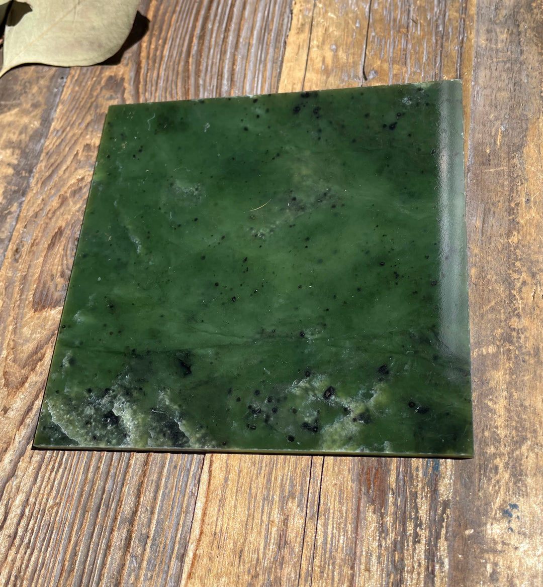 Single 4x4 Canadian Jade tile in deep green with black speckles on a wooden surface.