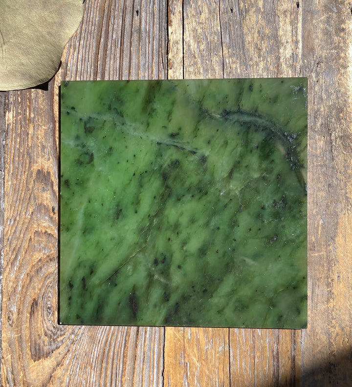 Single 4x4 inch dark green jade tile with lighter veining on a wooden surface.