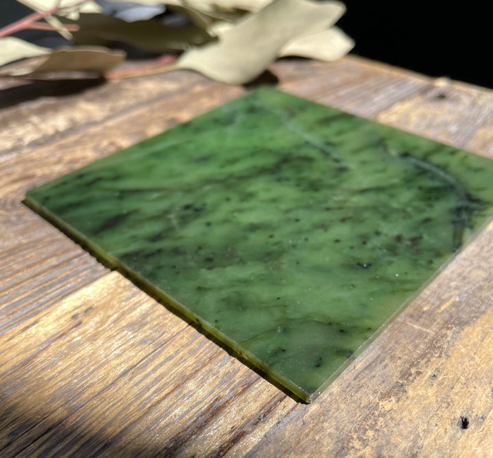 4x4 Canadian jade tile with rich green swirls and small dark specks on a rustic wood surface