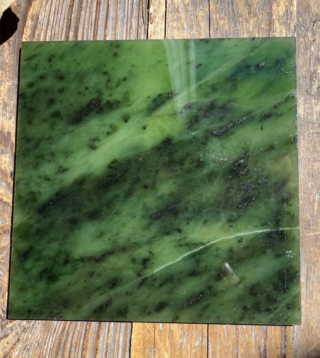Polished green jade tile with diagonal lighter banding and speckled pattern on a wooden backdrop
