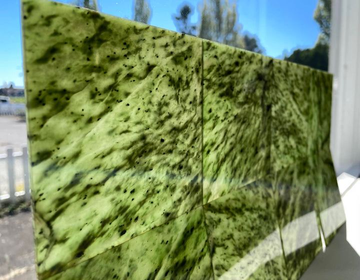 Several glossy green jade tiles forming a panel with vibrant emerald color and dark mineral speckles