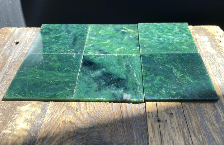 Six dark green Canadian Jade 2x2 inch tiles laid out on a wooden surface.