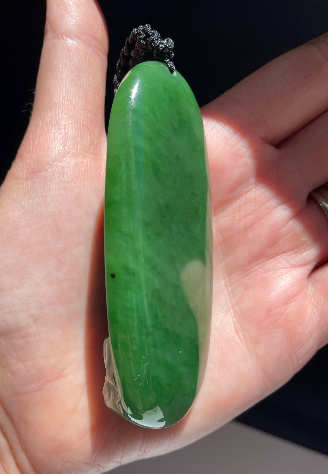Elongated green jade Buddha pendant held in a hand with a diamond ring visible