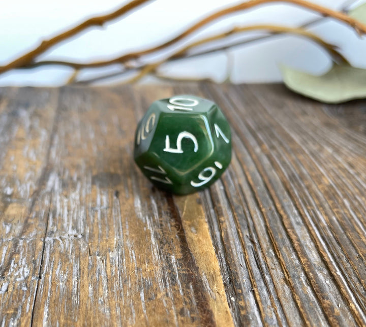 Green jade D12 die resting on a weathered wooden surface with white numerals