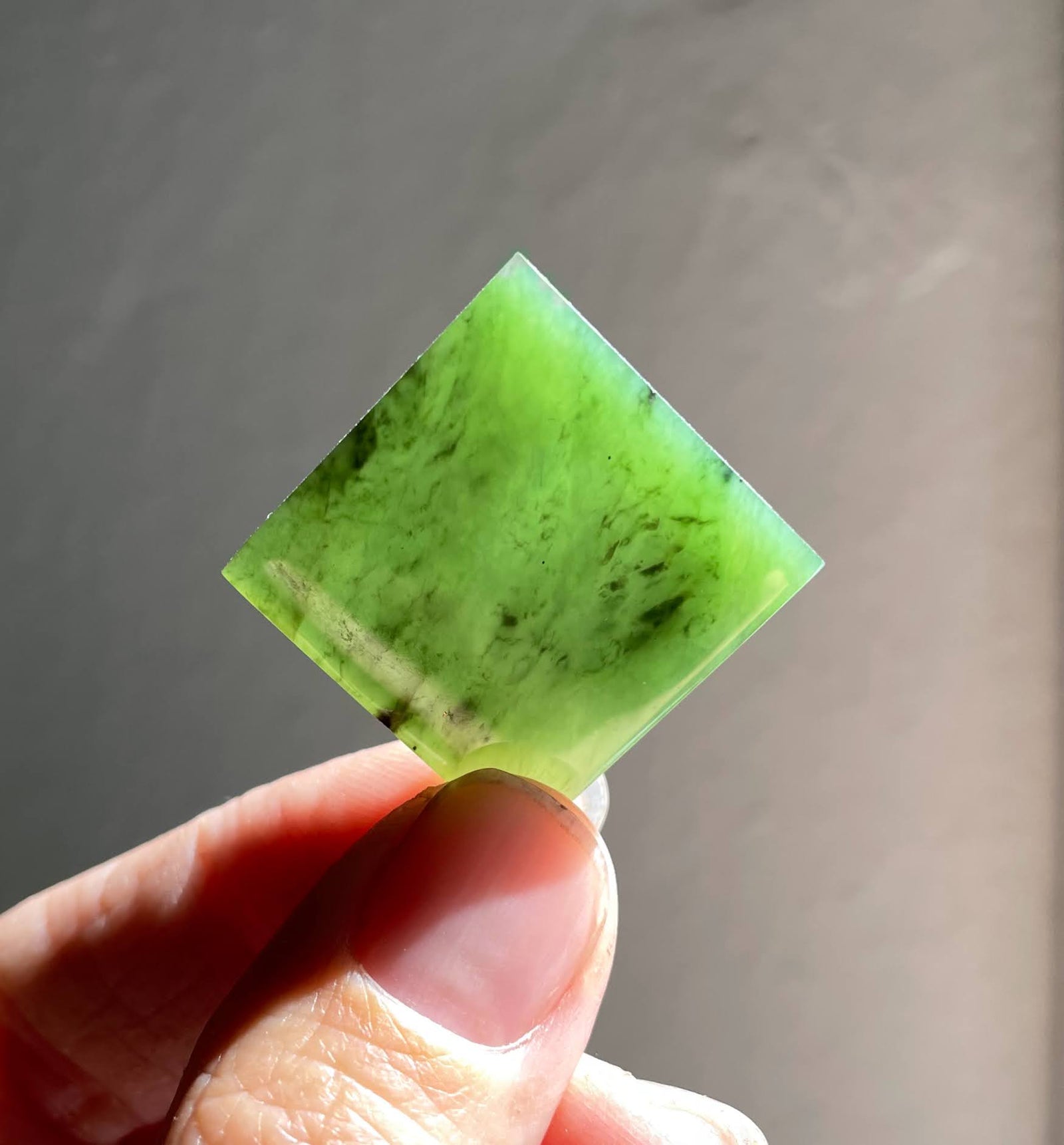 Translucent bright green jade square cabochon held between fingers