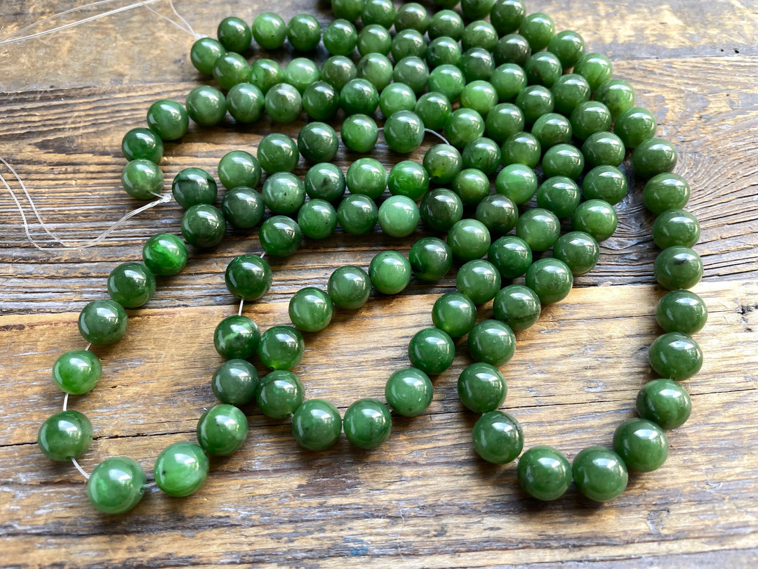 Unstrung green 10mm beads scattered on a rustic wooden surface with loose thread.
