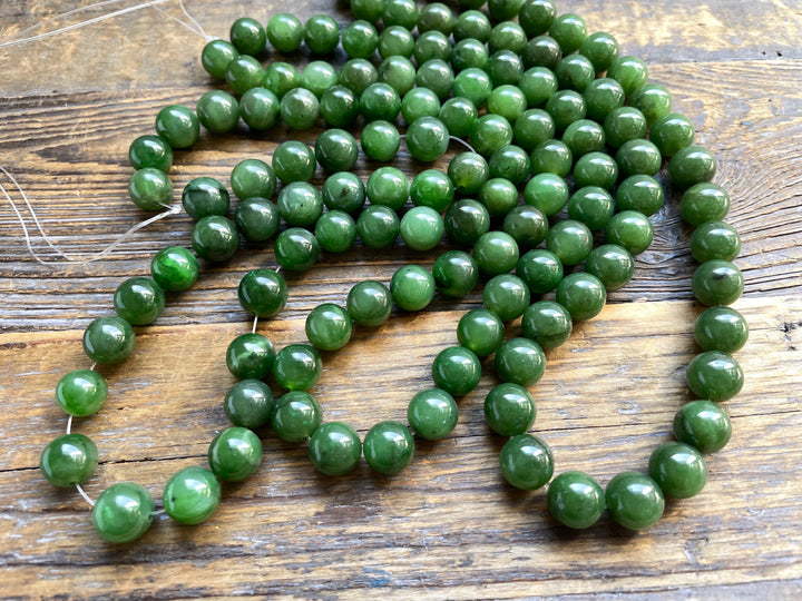 Unstrung green 10mm beads scattered on a rustic wooden surface with loose thread.